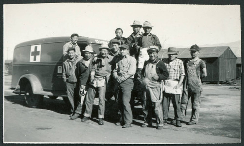 Photograph of a construction crew standing in front of a U.S. Army ambulance at Manzanar