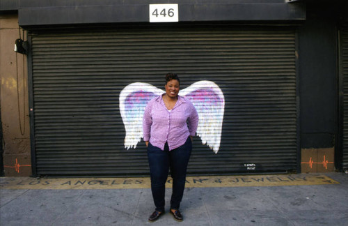 Unidentified woman in a red and white shirt posing in front of a mural depicting angel wings