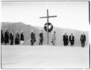 Dozen people standing in a line before a cross and wreath for a funeral