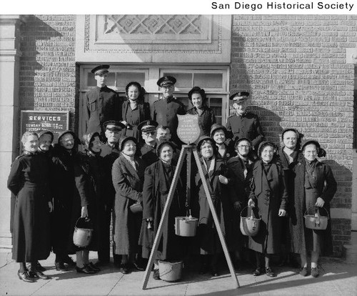 Members of the Salvation Army standing in front of a building with their traditional fundraising kettle