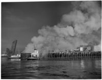 Smoke rises over L.A. Harbor while a coast guard boat battles the fire that began when the Markay oil tanker exploded, Los Angeles, 1947