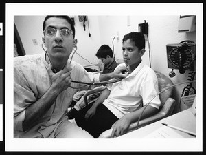 Man using stethoscope on a child at the UMMA Free Clinic, Los Angeles, 1999