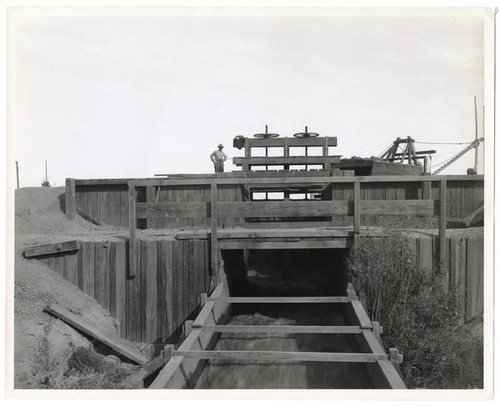 Man standing atop a small wooden dam, circa 1909