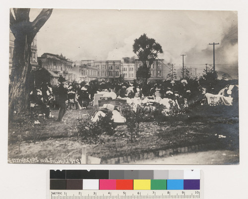 [Early gathering of refugees in unidentified park. Fire burning in background.]