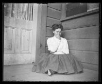 Woman seated in corner of porch, next to door