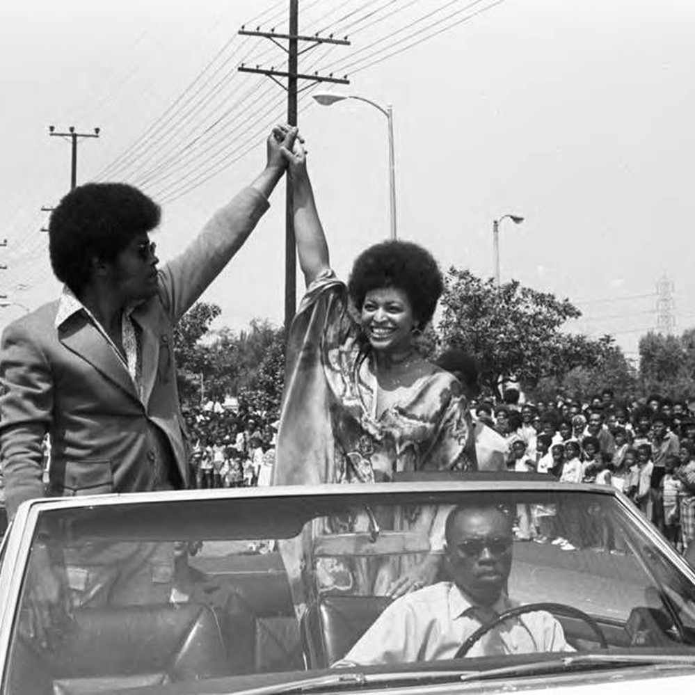 Clarence Williams, III and Gloria Foster riding in a Watts Summer Festival  parade, Los Angeles, ca. 1971 — Calisphere, image size:999x999